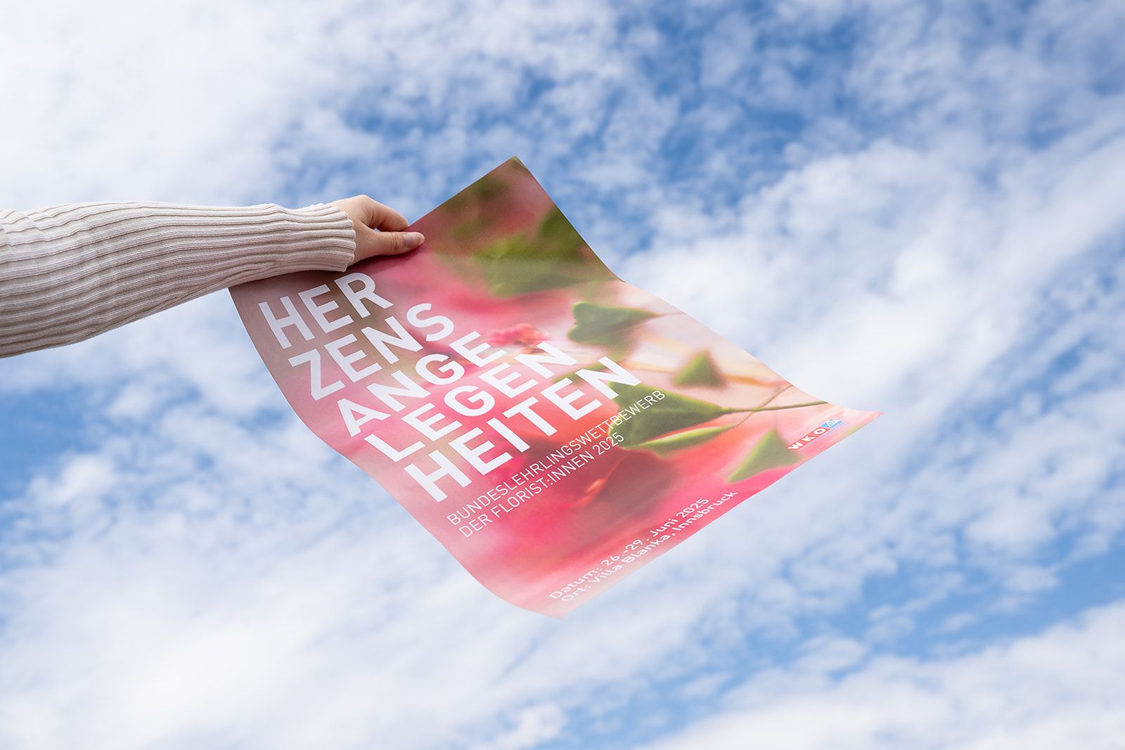 Hand hält das Plakat „Herzensangelegenheiten“ vor einen Himmel mit Wolken